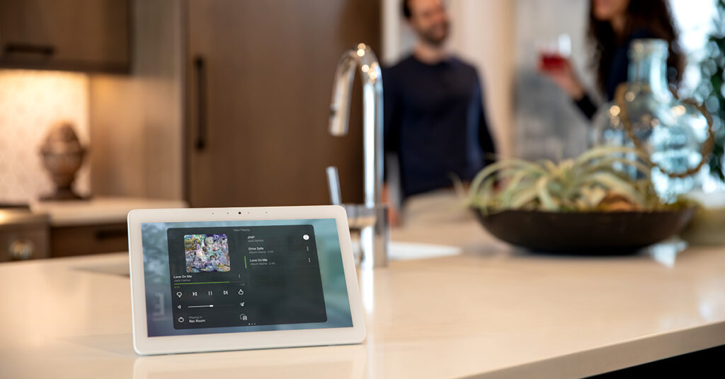 smart-home wireless touchscreen sits on kitchen counter while family enjoy themselves in the background